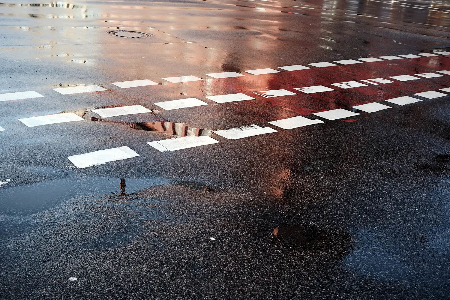 das Steglitzer Schloss spiegelt sich rot auf der regennassen Fahrbahn