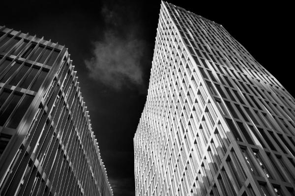 Two modern high-rise office buildings photographed from below against a dark sky in black and white, showing geometric archit